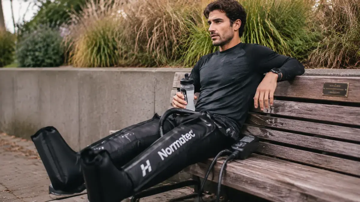 Person sitting on a bench after a run with air compression recovery boots on both legs