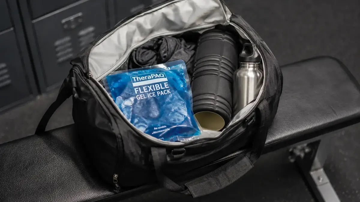 Reusable gel ice pack resting on a gym bag beside a water bottle and foam roller on a locker room bench