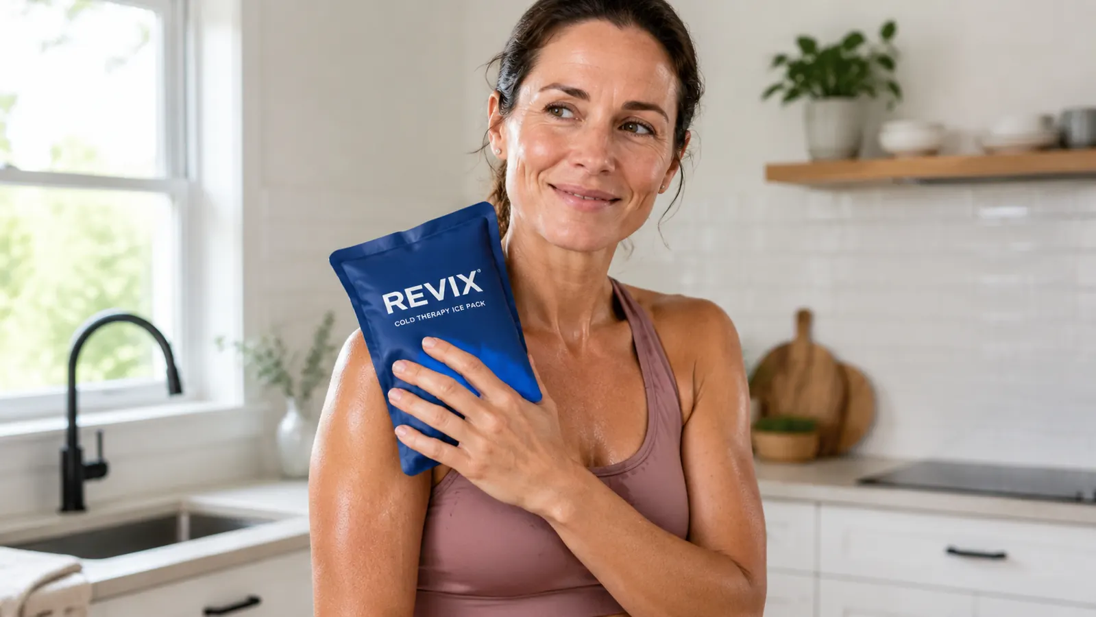 Reusable ice pack being placed on a shoulder by a person in workout clothes, standing in a kitchen