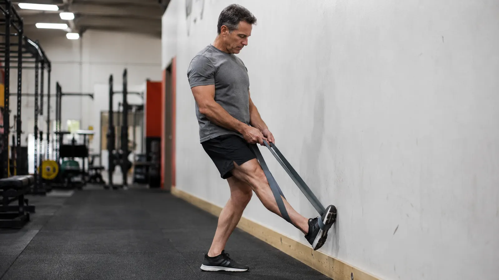 Person using the OPTP strap for a standing calf stretch against a wall in a gym setting