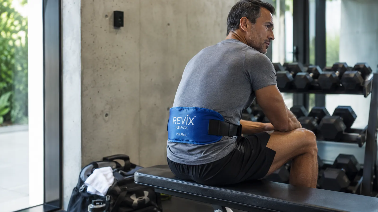 REVIX gel ice pack strapped to a person's lower back while sitting on a gym bench